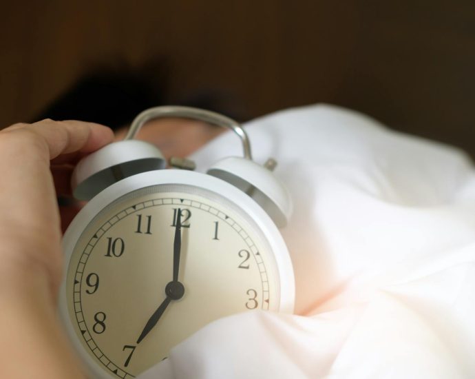 A close-up of a hand reaching for a ringing alarm clock, symbolizing waking up in the morning.