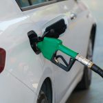 Close-up of a green nozzle refueling a white car at a gas station.