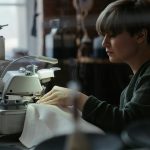 Woman using an overlock machine in a sewing workshop, showcasing concentration and craftsmanship.