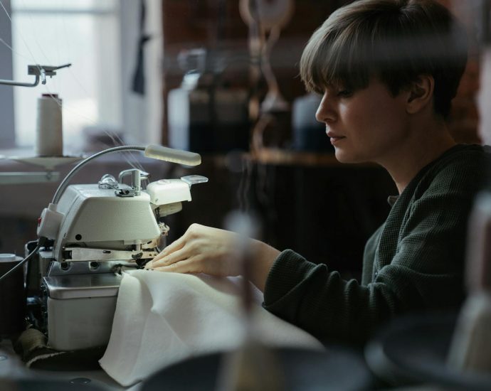 Woman using an overlock machine in a sewing workshop, showcasing concentration and craftsmanship.