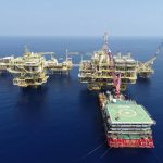 Aerial shot of multiple offshore oil platforms in a serene, blue sea under clear skies.