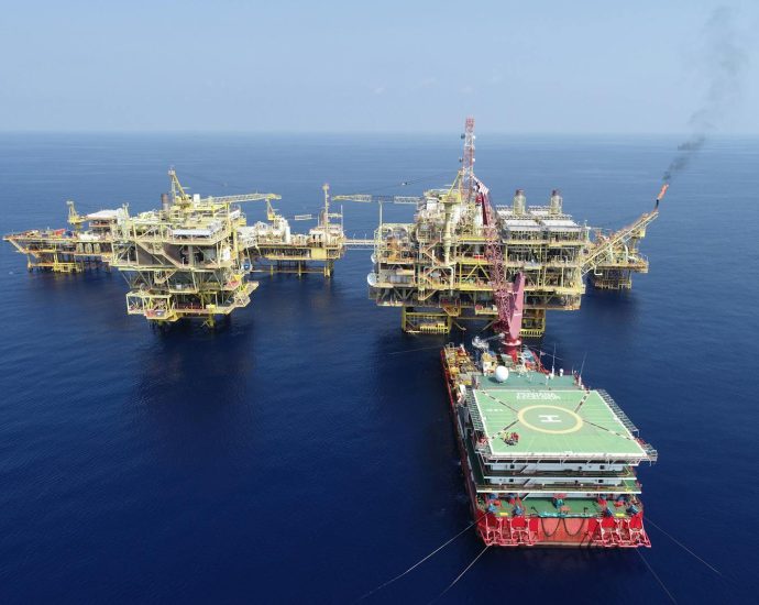 Aerial shot of multiple offshore oil platforms in a serene, blue sea under clear skies.