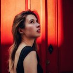 Woman looks up, illuminated by a striking red light.