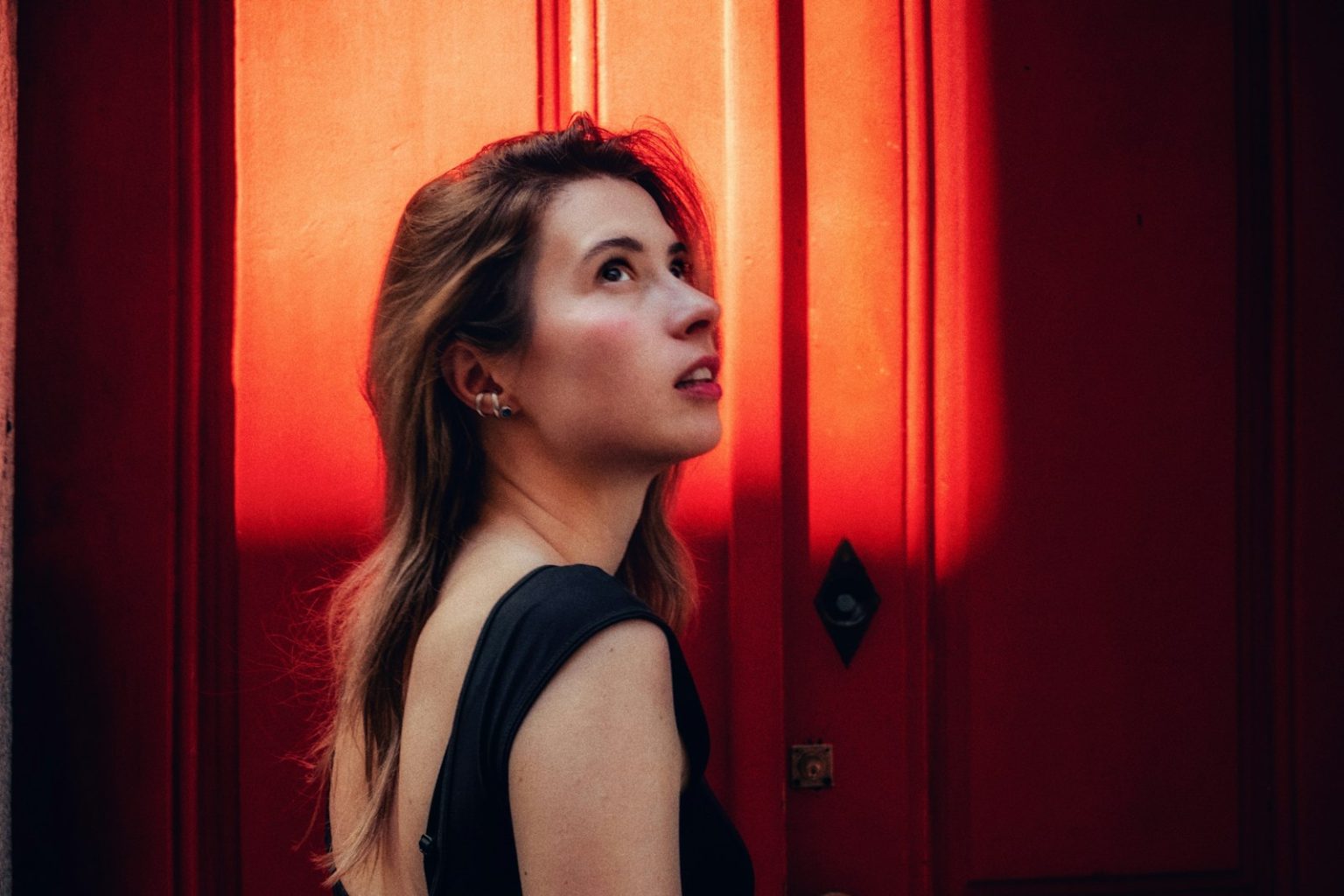 Woman looks up, illuminated by a striking red light.