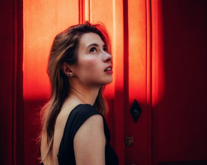 Woman looks up, illuminated by a striking red light.