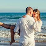 Young couple enjoying a romantic moment on a sunny beach, with waves in the background.