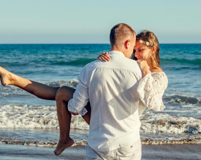 Young couple enjoying a romantic moment on a sunny beach, with waves in the background.