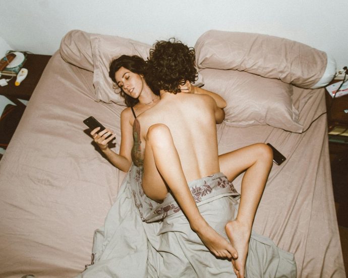 A couple in bed looking at smartphones, highlighting modern disconnection.