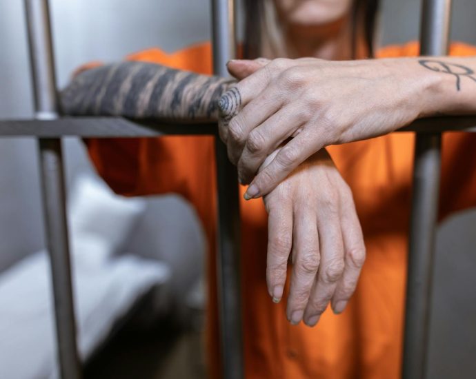 Close-up of tattooed hands behind jail bars, illustrating incarceration and confinement.