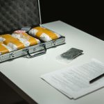 Briefcase with packages and documents on a table, suggesting illegal activity or crime scene investigation.
