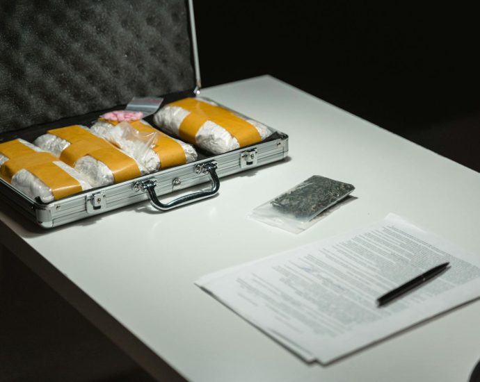 Briefcase with packages and documents on a table, suggesting illegal activity or crime scene investigation.