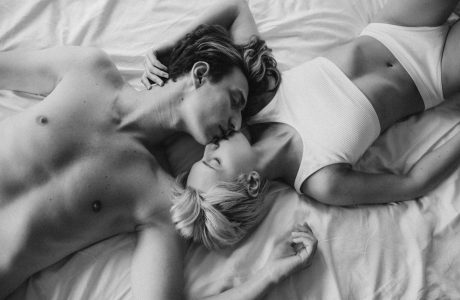 Black and white photo of a couple kissing and embracing on a bed, showcasing intimacy.