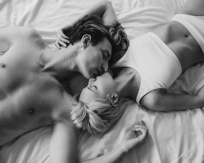 Black and white photo of a couple kissing and embracing on a bed, showcasing intimacy.