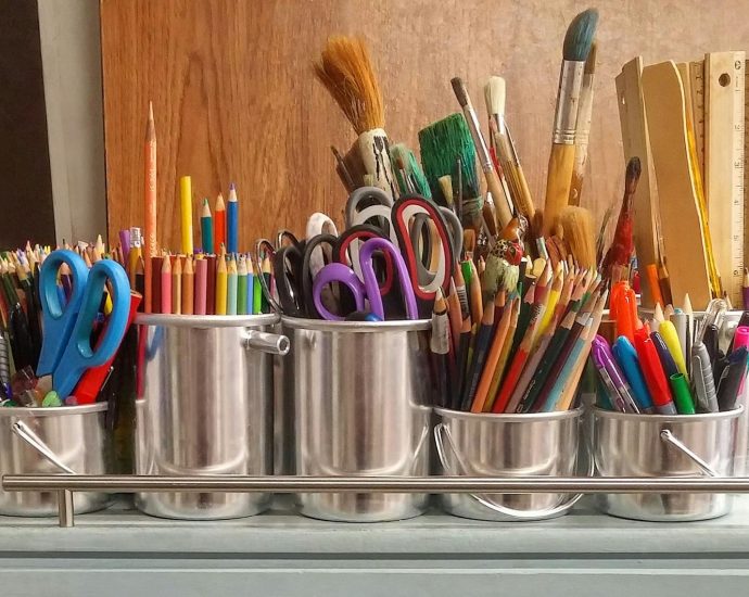 A diverse collection of art supplies in metallic buckets on a wooden table.