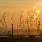Silhouette of power lines and industrial smoke at sunset, highlighting pollution and energy themes.