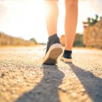 A woman walks down a sunlit path in summer, highlighting leisure and travel outdoors.