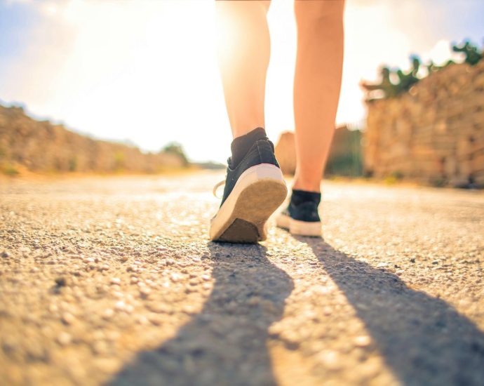 A woman walks down a sunlit path in summer, highlighting leisure and travel outdoors.