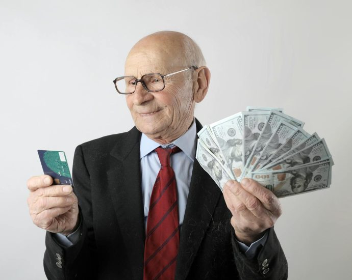 Elderly man in a suit holding a credit card and US dollar bills, representing finance and wealth.