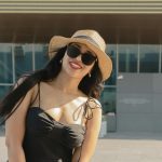 Woman in hat and sunglasses smiles outdoors