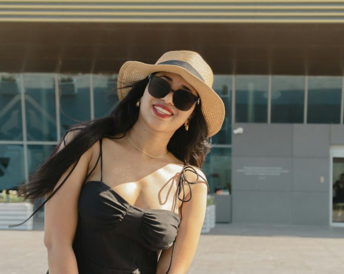 Woman in hat and sunglasses smiles outdoors