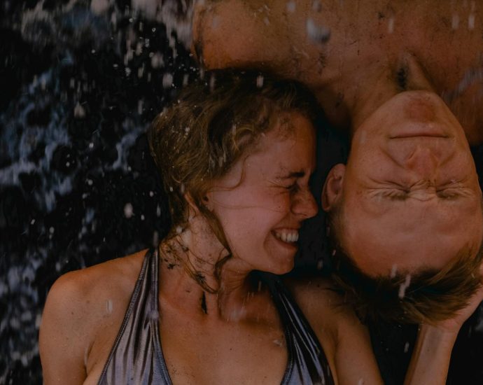 Joyful couple embracing beach waves, eyes closed, under summer sun.