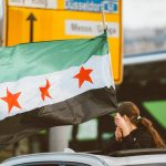 A woman holding a flag on top of a car