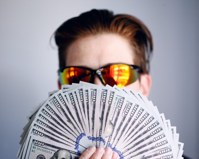 man in black framed sunglasses holding fan of white and gray striped cards