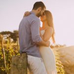 A couple shares a romantic moment embracing at sunset outdoors with warm light.