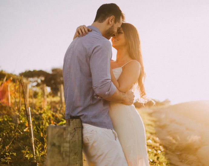 A couple shares a romantic moment embracing at sunset outdoors with warm light.