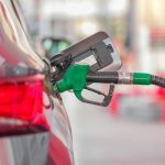 A close-up view of a fuel pump nozzle inserted into a car's tank at a gas station.