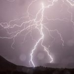 Captivating lightning bolts illuminate the night sky over dark hills in a dramatic weather display.