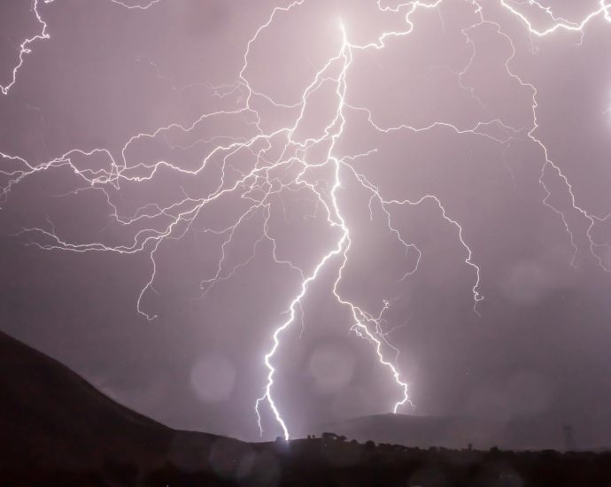 Captivating lightning bolts illuminate the night sky over dark hills in a dramatic weather display.