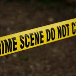 Close-up of crime scene tape with 'Do Not Cross' text, outdoors setting.