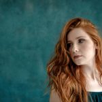 Young woman with long red hair against teal background