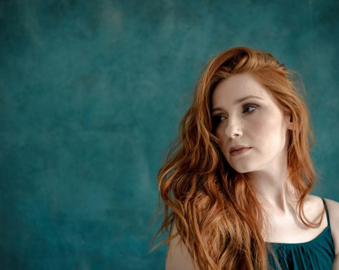 Young woman with long red hair against teal background
