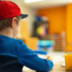 a young boy sitting at a table writing on a piece of paper