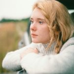 A woman with braided blonde hair gazes thoughtfully from a car window, capturing a serene moment.