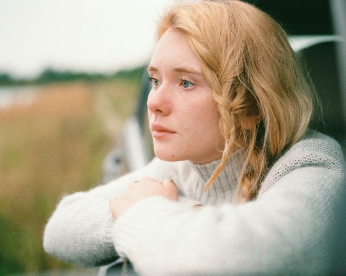 A woman with braided blonde hair gazes thoughtfully from a car window, capturing a serene moment.