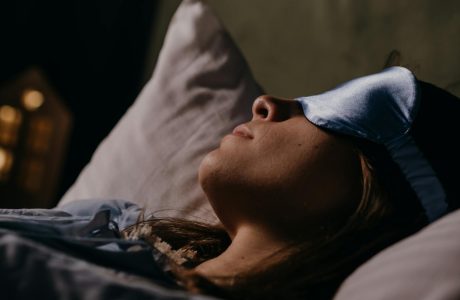 A serene scene of a woman wearing a blue eye mask, sleeping soundly in a cozy indoors setting.