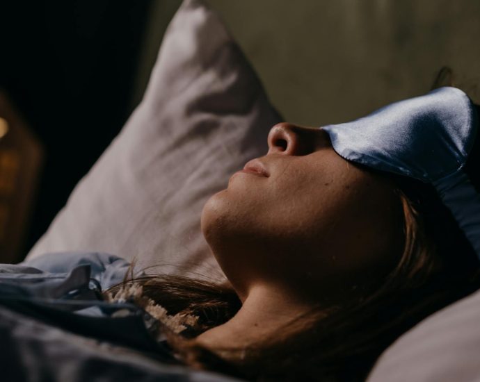 A serene scene of a woman wearing a blue eye mask, sleeping soundly in a cozy indoors setting.