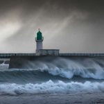 a lighthouse on a pier with waves crashing in front of it