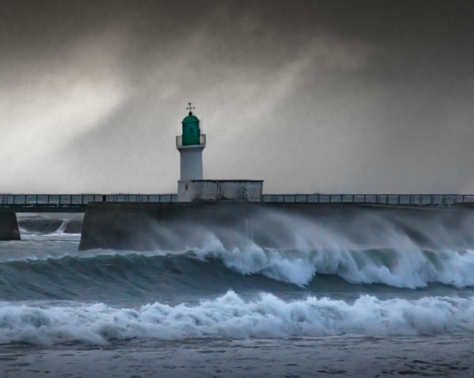 a lighthouse on a pier with waves crashing in front of it