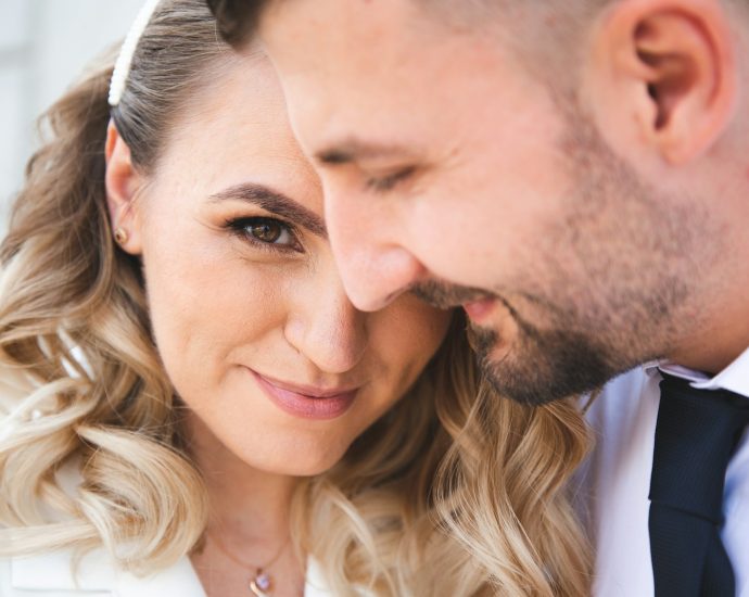 A couple embraces closely, looking at the camera