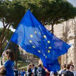a young girl holding a european flag in front of a crowd of people