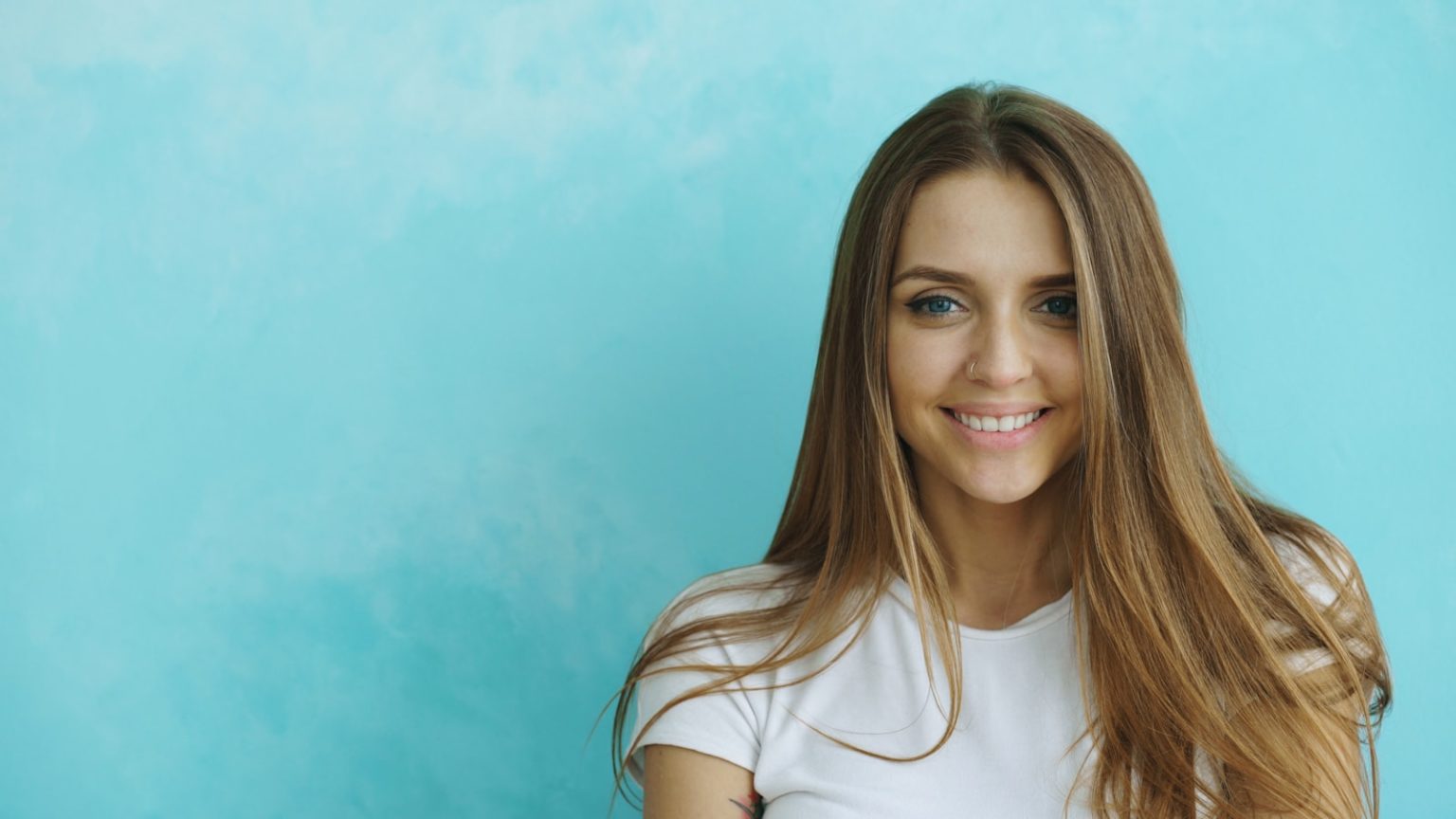 Young woman smiles against a blue textured wall