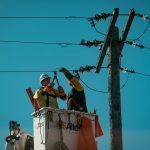 Electricians in safety gear working on power lines in bright daylight. Energy industry focus.
