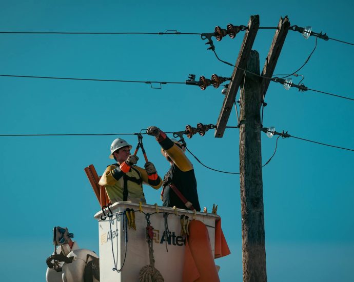 Electricians in safety gear working on power lines in bright daylight. Energy industry focus.