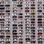 Top-down aerial shot of a large parking lot filled with rows of cars, showcasing organized symmetry.