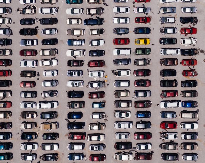 Top-down aerial shot of a large parking lot filled with rows of cars, showcasing organized symmetry.