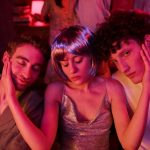 Three friends in neon lighting enjoying a vibrant night out, embracing together in a relaxed atmosphere.